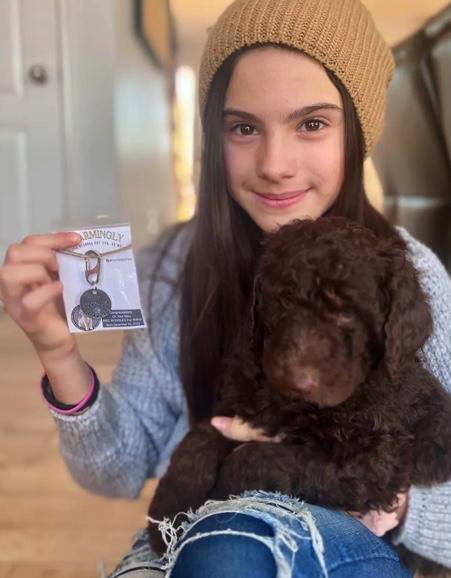 Brynlie holding her dog and one of her custom dog tags in a package